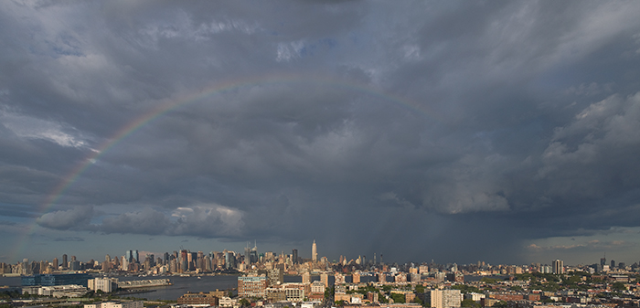 rainbow arching up from left side, ending in swirling clouds. rain showers shoot down behind empire state building