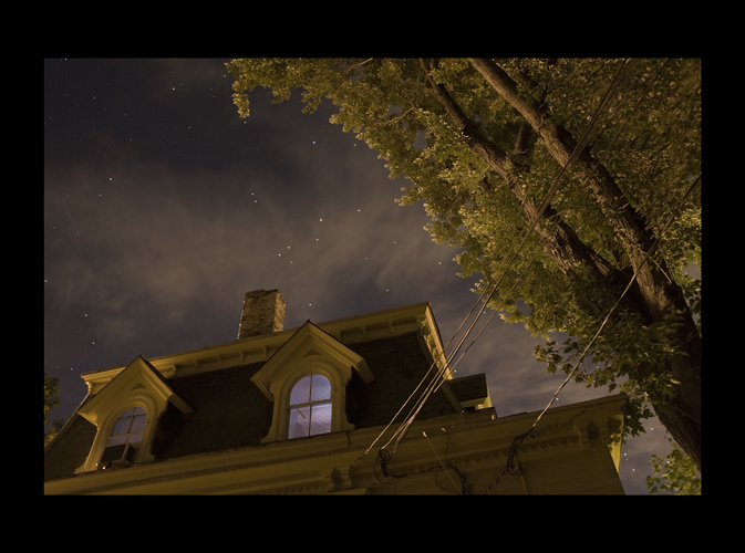 a room lit by a tv. outside tree and house theatrically lit by streetlight. stars and clouds